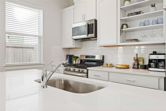 kitchen with open shelves, stainless steel appliances, light countertops, and a sink