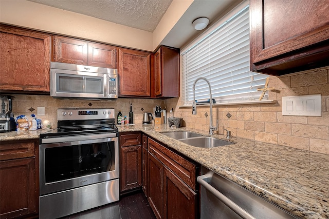 kitchen featuring light stone counters, a sink, stainless steel appliances, a textured ceiling, and tasteful backsplash