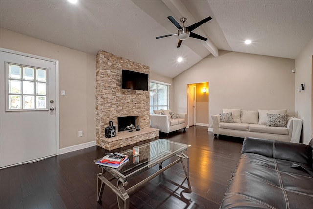 living room featuring a textured ceiling, dark wood-style floors, a stone fireplace, baseboards, and vaulted ceiling with beams