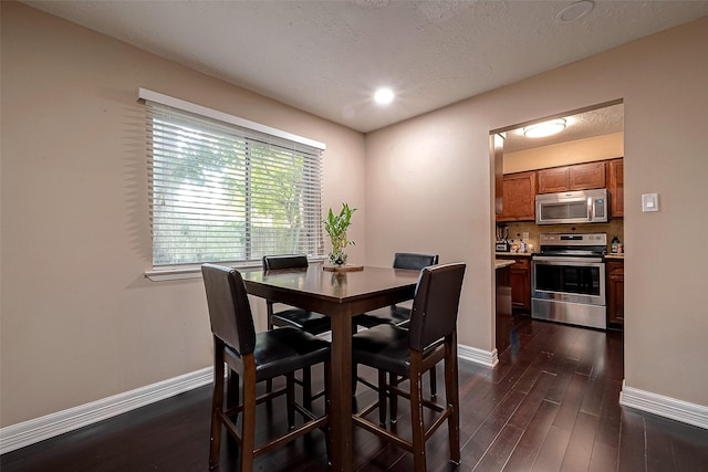 dining space with a textured ceiling, baseboards, and dark wood-style flooring