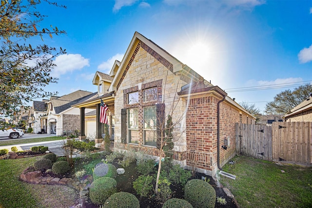 view of home's exterior with fence, a garage, stone siding, a lawn, and brick siding