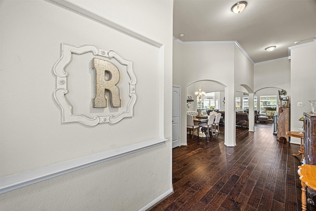 hallway featuring ornamental molding, hardwood / wood-style flooring, arched walkways, an inviting chandelier, and baseboards