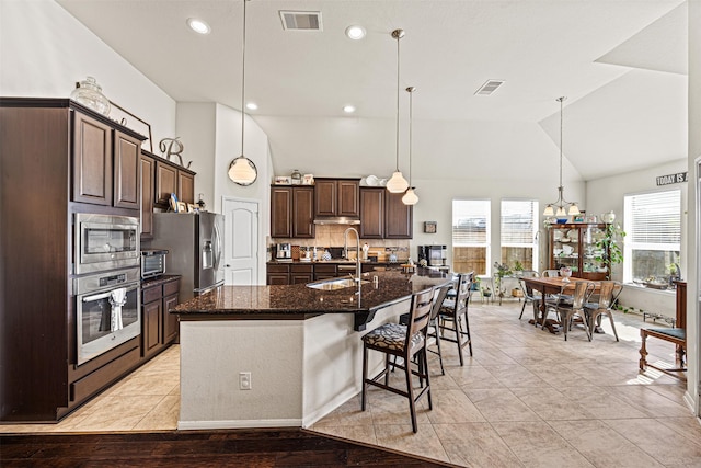 kitchen featuring visible vents, a sink, dark brown cabinetry, appliances with stainless steel finishes, and a kitchen bar