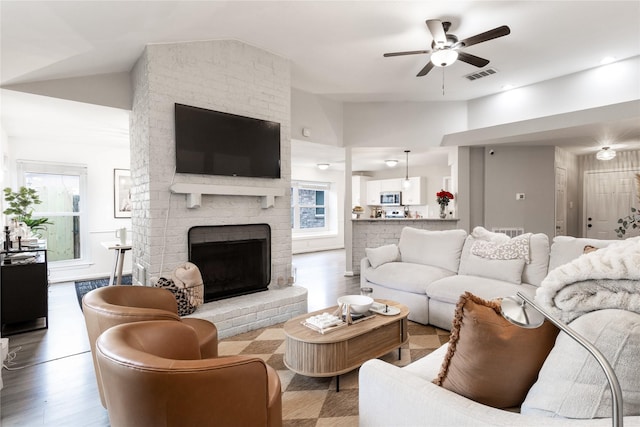 living room featuring visible vents, a brick fireplace, ceiling fan, vaulted ceiling, and wood finished floors