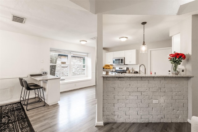 kitchen featuring visible vents, a peninsula, wood finished floors, white cabinets, and stainless steel appliances