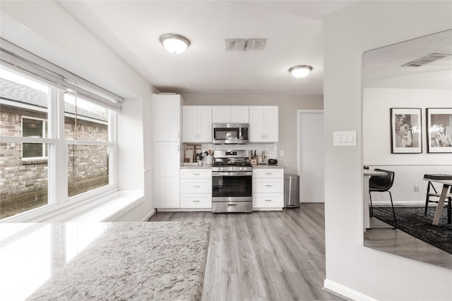 kitchen with decorative backsplash, white cabinets, visible vents, and stainless steel appliances