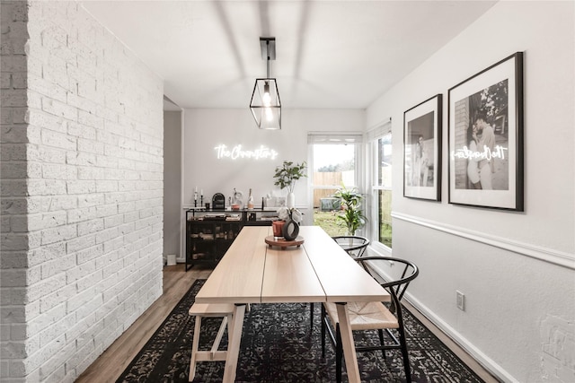 dining space featuring dark wood-style floors, brick wall, indoor bar, and baseboards