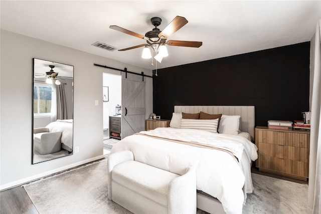 bedroom with visible vents, baseboards, a barn door, wood finished floors, and a ceiling fan