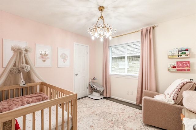 bedroom featuring wood finished floors, baseboards, a crib, and a chandelier