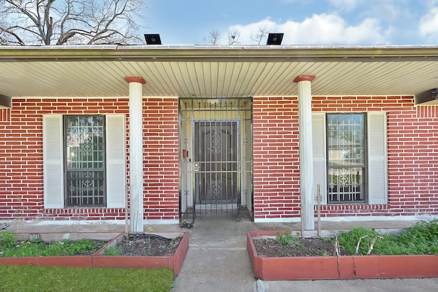 view of exterior entry with covered porch and brick siding