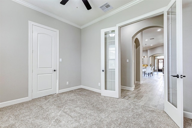 empty room featuring visible vents, carpet floors, ornamental molding, french doors, and arched walkways