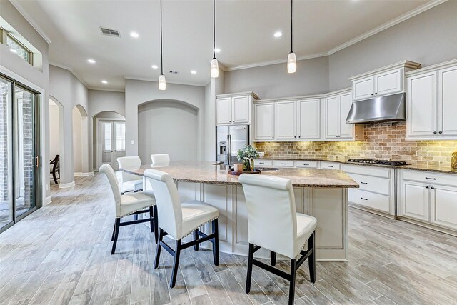 kitchen featuring under cabinet range hood, appliances with stainless steel finishes, tasteful backsplash, and wood tiled floor