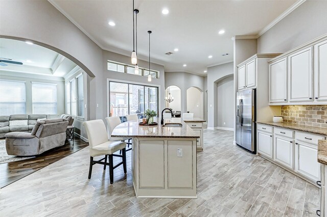 kitchen with backsplash, light stone countertops, an island with sink, light wood-style flooring, and stainless steel refrigerator with ice dispenser