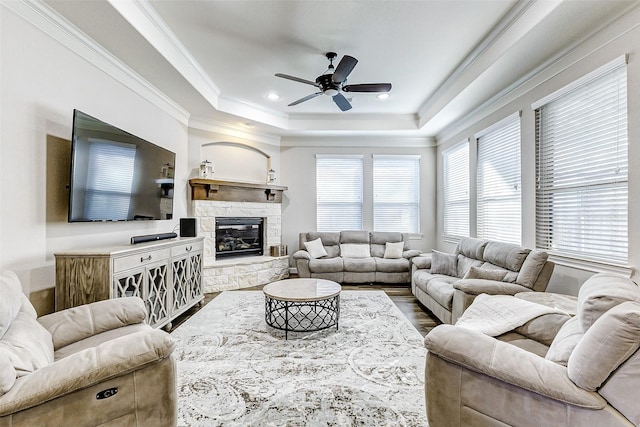 living area with dark wood-type flooring, a tray ceiling, ornamental molding, a fireplace, and a ceiling fan