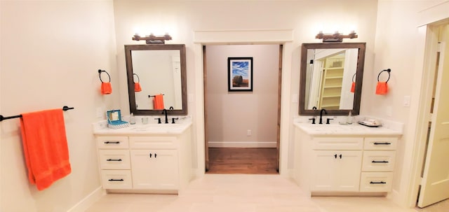 full bathroom with a sink, baseboards, and two vanities