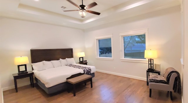 bedroom featuring light wood-style flooring, a raised ceiling, and baseboards