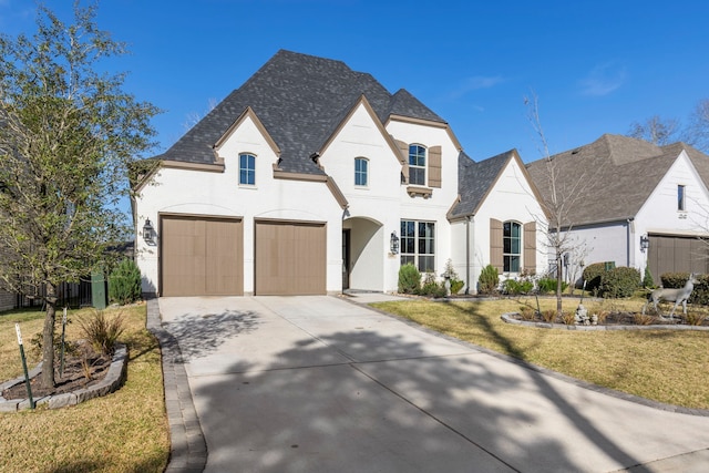 french country inspired facade with concrete driveway, a garage, and a front lawn