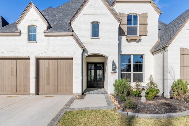 exterior space featuring concrete driveway, french doors, brick siding, and a shingled roof