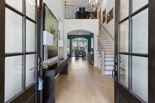 entryway with stairway, light wood finished floors, a high ceiling, arched walkways, and a chandelier