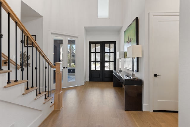 foyer featuring stairway, french doors, light wood-type flooring, and a towering ceiling