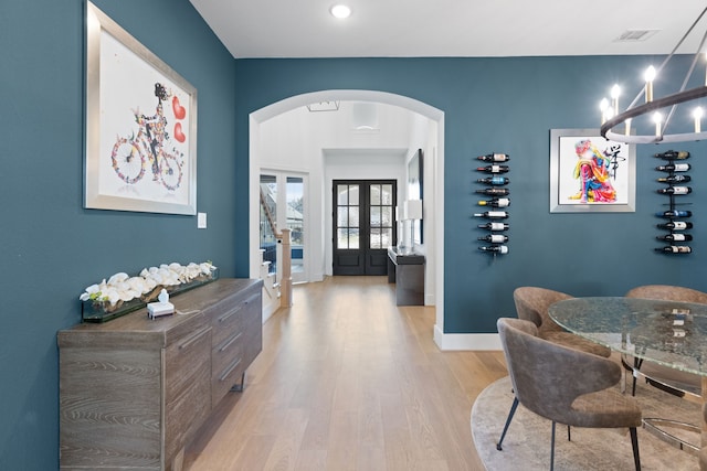 interior space with visible vents, baseboards, french doors, light wood-style floors, and arched walkways