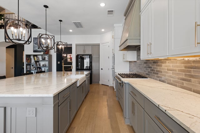 kitchen with visible vents, light wood-type flooring, custom exhaust hood, gray cabinetry, and tasteful backsplash