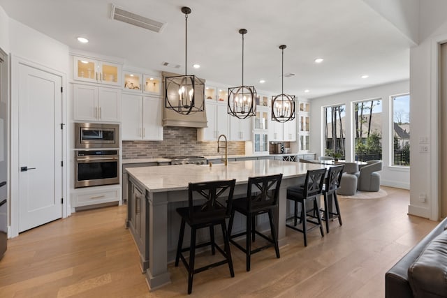 kitchen with visible vents, a sink, stainless steel appliances, light wood-style floors, and backsplash