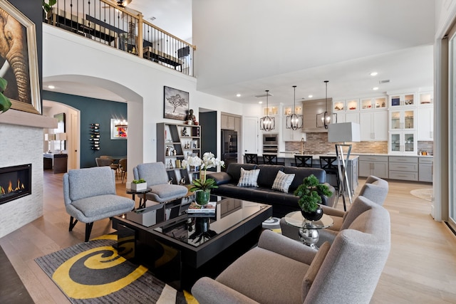 living area featuring a high ceiling, recessed lighting, arched walkways, a stone fireplace, and light wood-type flooring