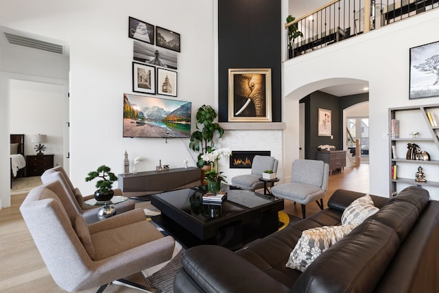 living room featuring arched walkways, visible vents, a warm lit fireplace, and wood finished floors