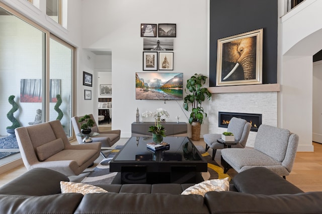 living room featuring a towering ceiling, a lit fireplace, and wood finished floors