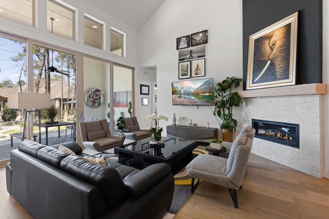 living area with a glass covered fireplace, high vaulted ceiling, a ceiling fan, and wood finished floors