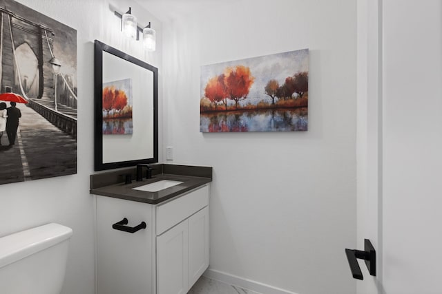 half bath with marble finish floor, toilet, vanity, and baseboards