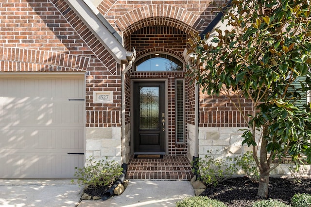 doorway to property featuring brick siding, stone siding, and an attached garage