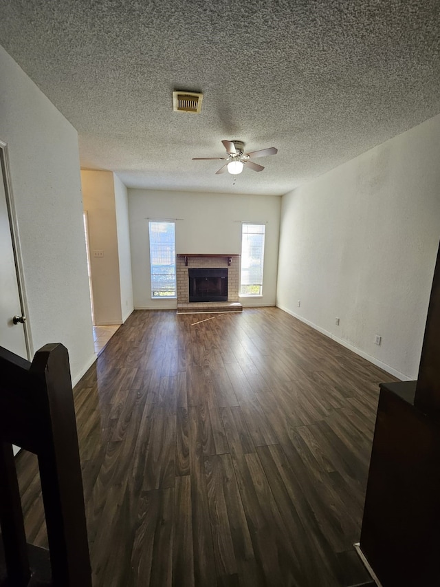 unfurnished living room featuring visible vents, a brick fireplace, ceiling fan, dark wood finished floors, and a textured ceiling