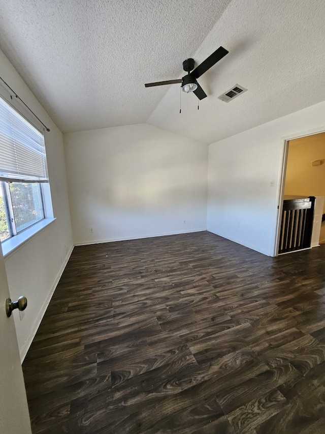 empty room featuring ceiling fan, visible vents, dark wood finished floors, and vaulted ceiling