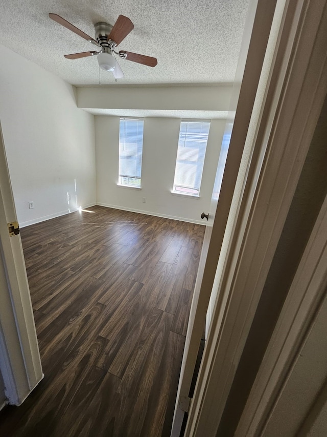 empty room featuring baseboards, dark wood-type flooring, a ceiling fan, and a textured ceiling