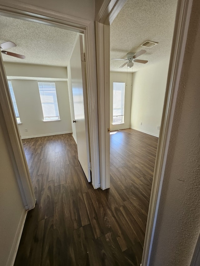 corridor with a wealth of natural light, visible vents, a textured ceiling, and dark wood-style floors