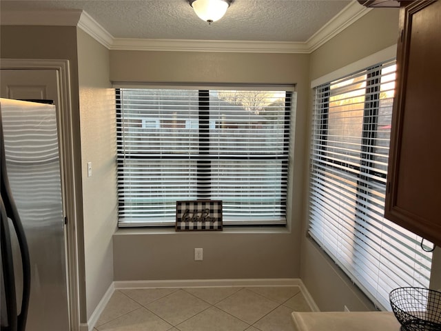 unfurnished dining area with light tile patterned floors, baseboards, a textured ceiling, and ornamental molding