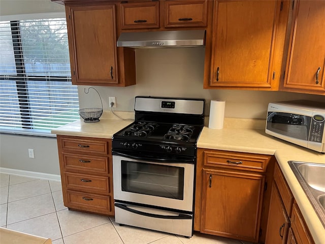 kitchen with under cabinet range hood, brown cabinets, stainless steel appliances, and light countertops