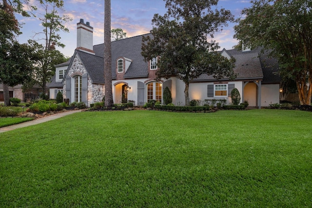 french country style house featuring a front lawn, stone siding, and a chimney