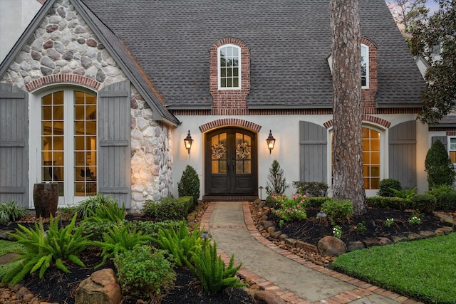 doorway to property featuring stone siding, french doors, and a shingled roof