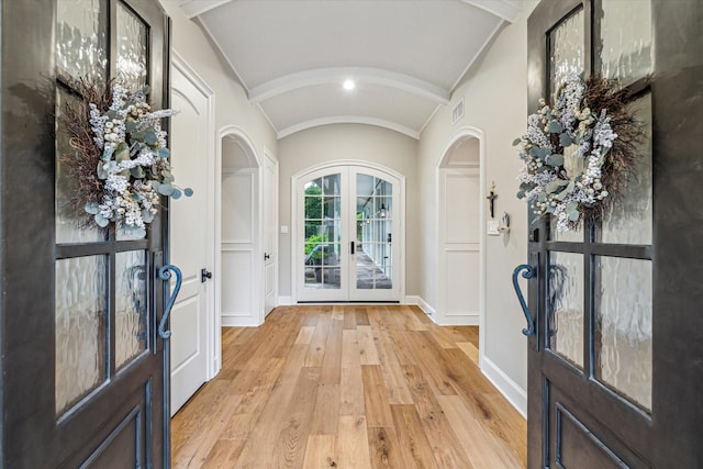 foyer entrance featuring baseboards, light wood-type flooring, lofted ceiling, french doors, and arched walkways