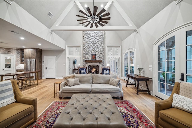 living area featuring visible vents, high vaulted ceiling, a stone fireplace, and light wood-style flooring