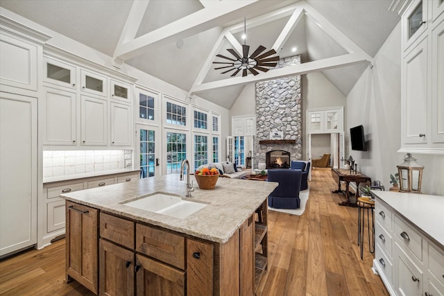 kitchen featuring a ceiling fan, a fireplace, a sink, glass insert cabinets, and light wood-style floors