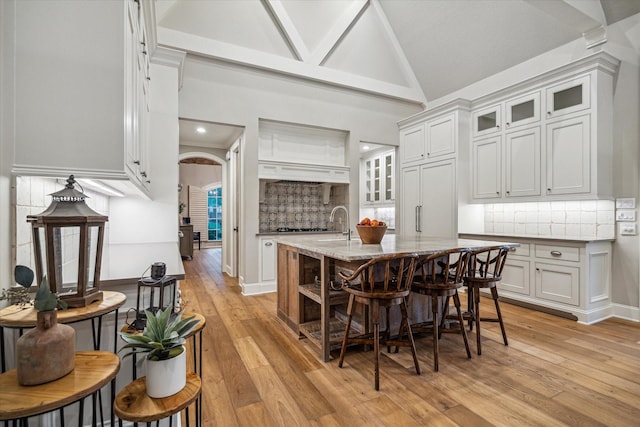 dining space featuring baseboards, arched walkways, high vaulted ceiling, and light wood-style flooring