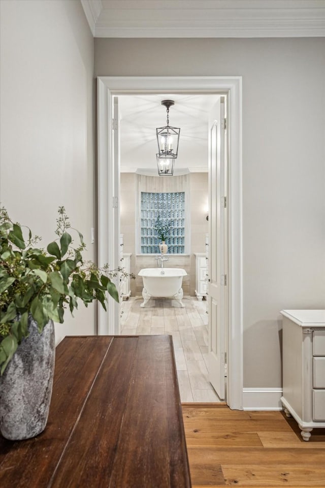 full bath with wood finished floors, baseboards, a freestanding tub, crown molding, and a chandelier