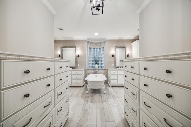 bathroom featuring visible vents, a freestanding tub, wood finish floors, and ornamental molding