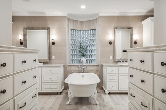 bathroom with wood tiled floor, two vanities, ornamental molding, a freestanding tub, and tile walls