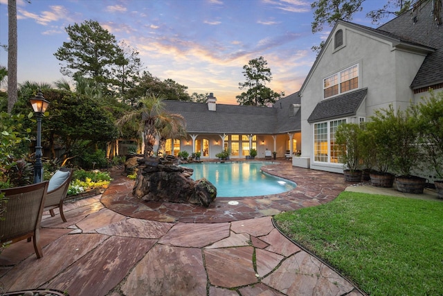 pool at dusk with a patio area, a lawn, and an outdoor pool