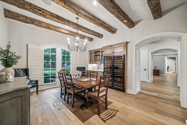 dining area with light wood finished floors, baseboards, wine cooler, arched walkways, and a notable chandelier